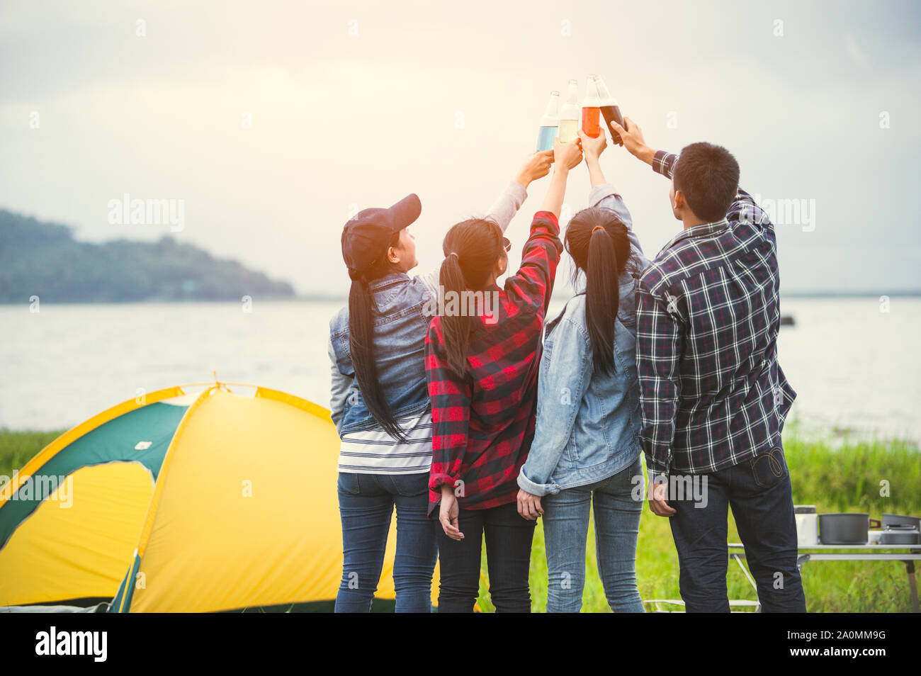 Back view of friendship clinking drinking bottle glass for celebrating in private party with mountain and lake view background. People lifestyle and t Stock Photo