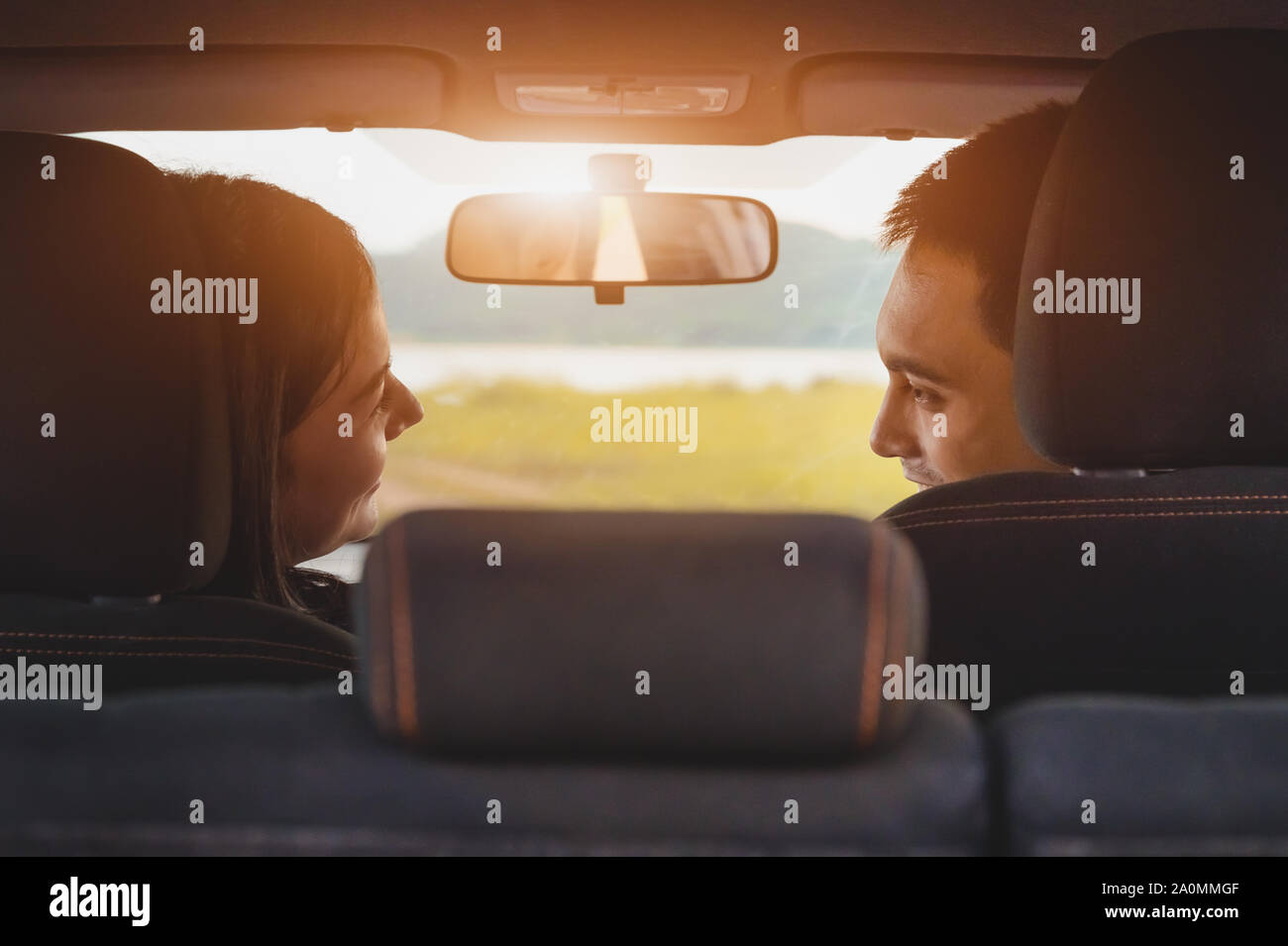 Back view of Asian couple looking each other in hatchback car at camping picnic place with green meadow and mountain. People lifestyles and transporta Stock Photo