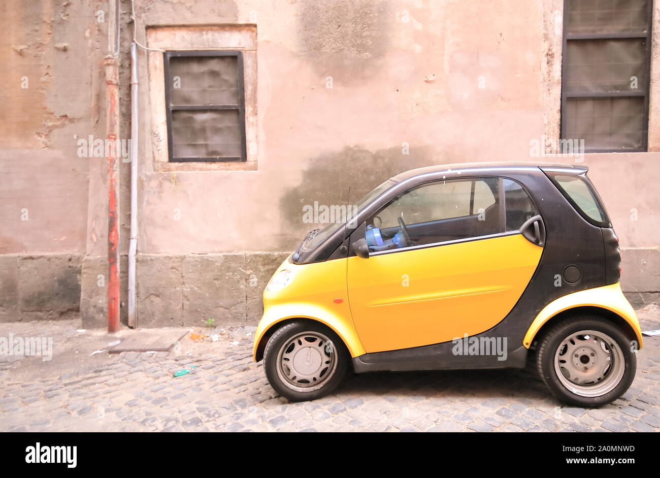 Small car parked on narrow alleyway in downtown Rome Italy Stock Photo