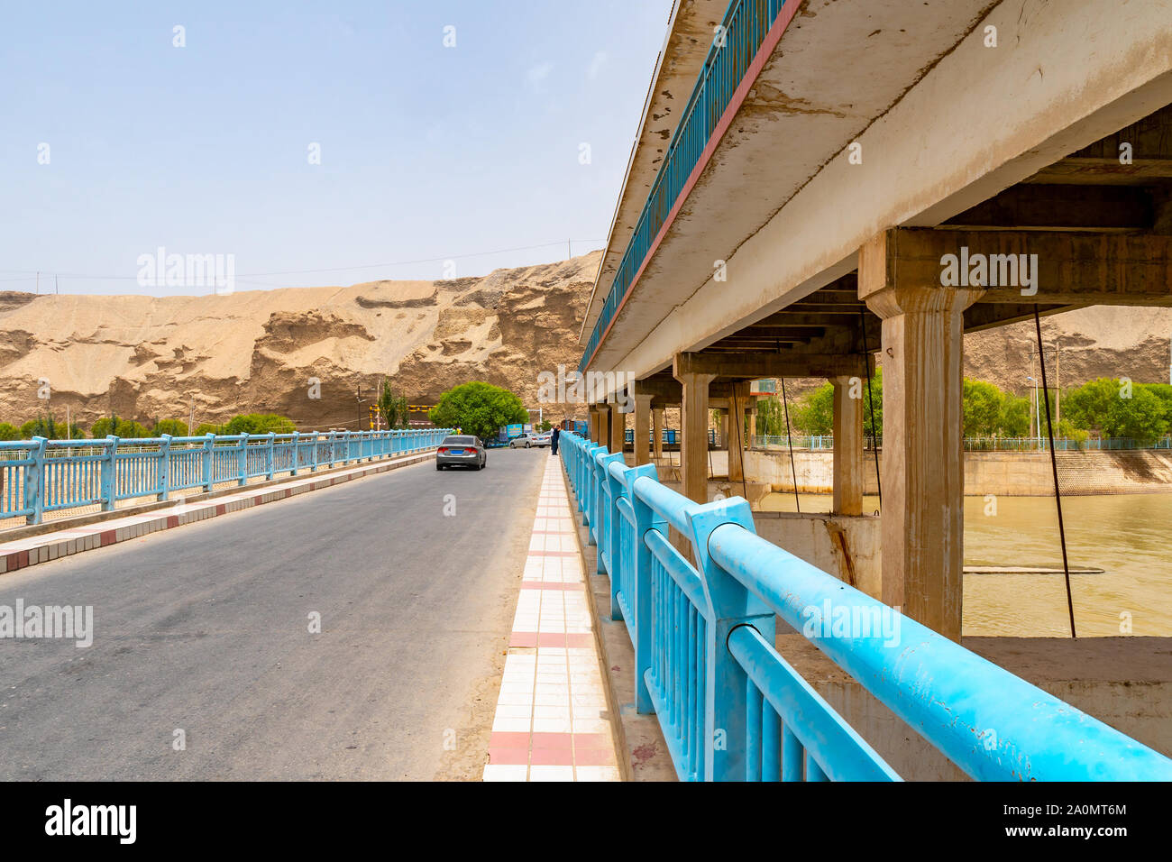 Karakash Black Jade River Dam View of Cars Driving over the Bridge on a Sunny Blue Sky Day Stock Photo