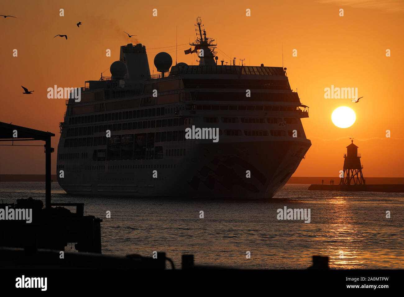 Sunrise as the Pacific Princess Cruise ship enters the Tyne, passing the Herd Groyne lighthouse at South Shields on the River Tyne estuary on the North East coast as temperatures are expected to soar to 26C in some parts of the country this weekend. Stock Photo