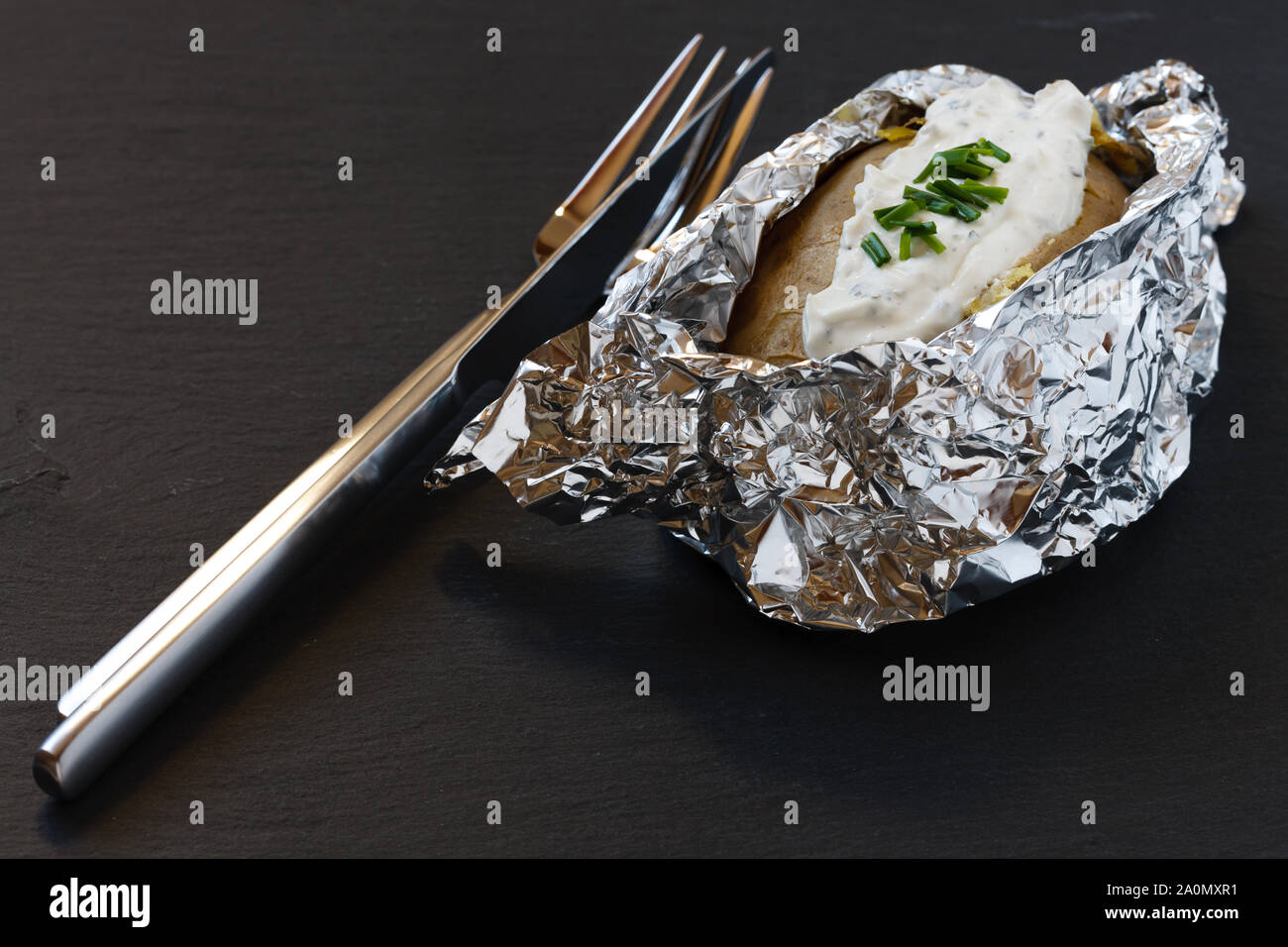 oven baked Potato in tin foil with Herbal Cream Cheese on slate board