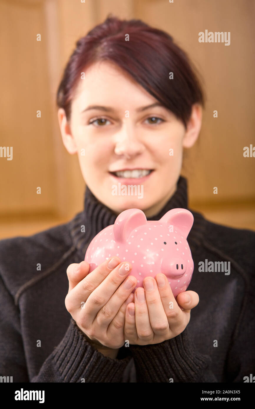 Young woman with her savings in a pink piggy bank Stock Photo