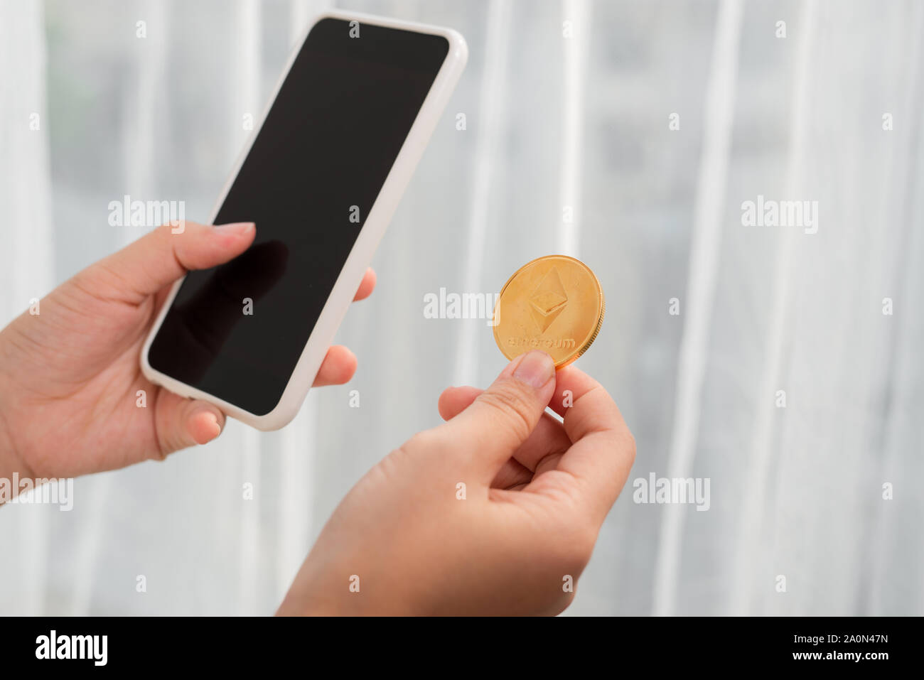 Holding crypto coin and mobile phone on white background Stock Photo