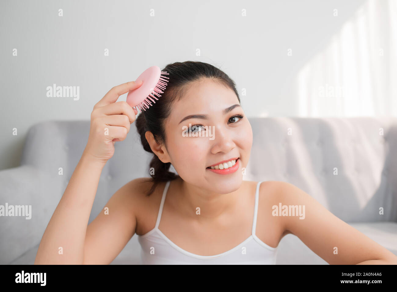 Portrait of beautiful young woman combing her hair, looking at camera and smiling Stock Photo