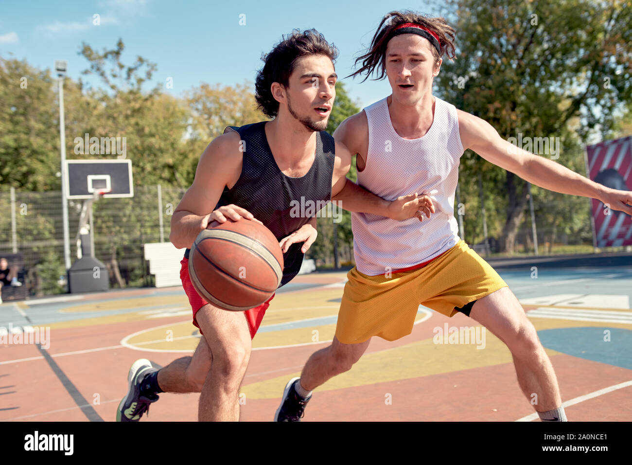 Picture of young sports men playing basketball on playground on summer day against background of green trees Stock Photo