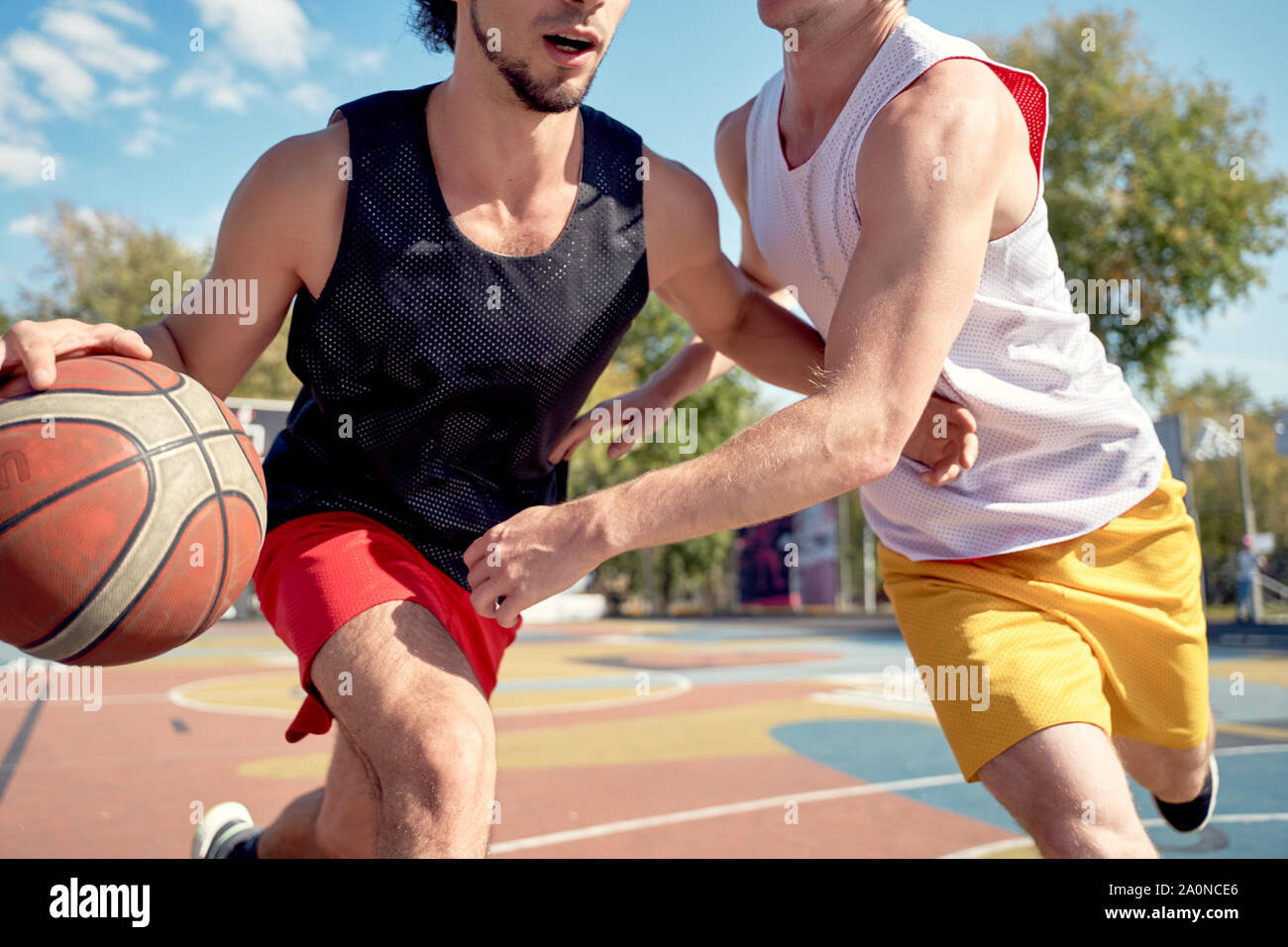 Photo of sportsmen playing basketball on playground on summer day against background of green trees Stock Photo