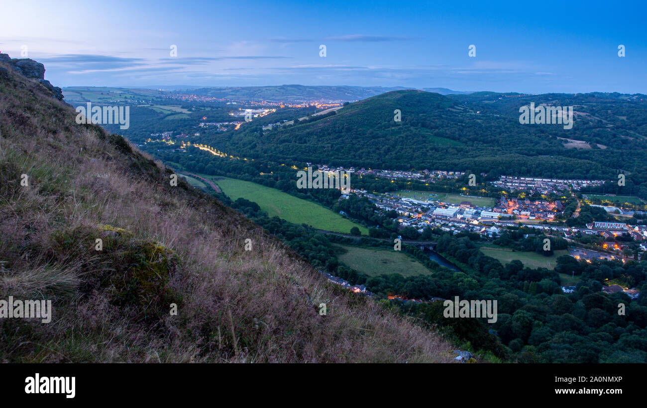 Lights of the towns of Taff's Well and Caerphilly and the A470 road illuminate the landscape of the South Wales valleys and hills at dusk. Stock Photo