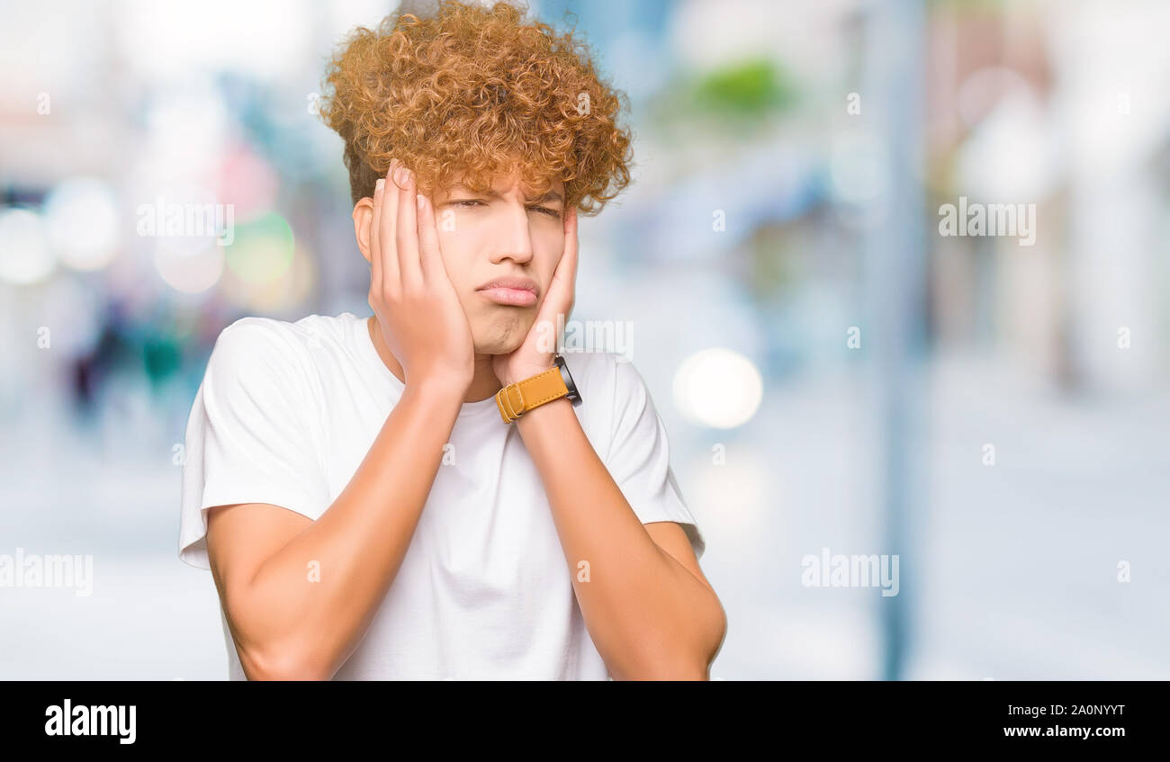 Young handsome man with afro hair wearing casual white t-shirt Tired ...