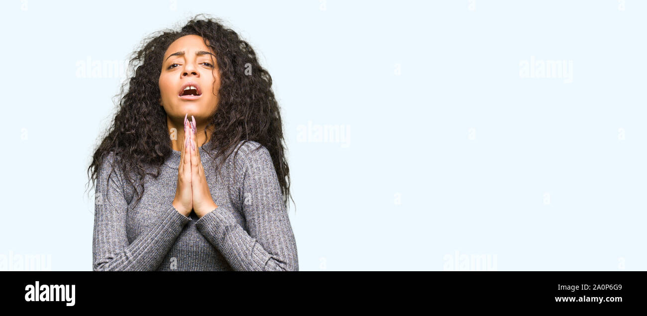 Young beautiful girl with curly hair begging and praying with hands ...