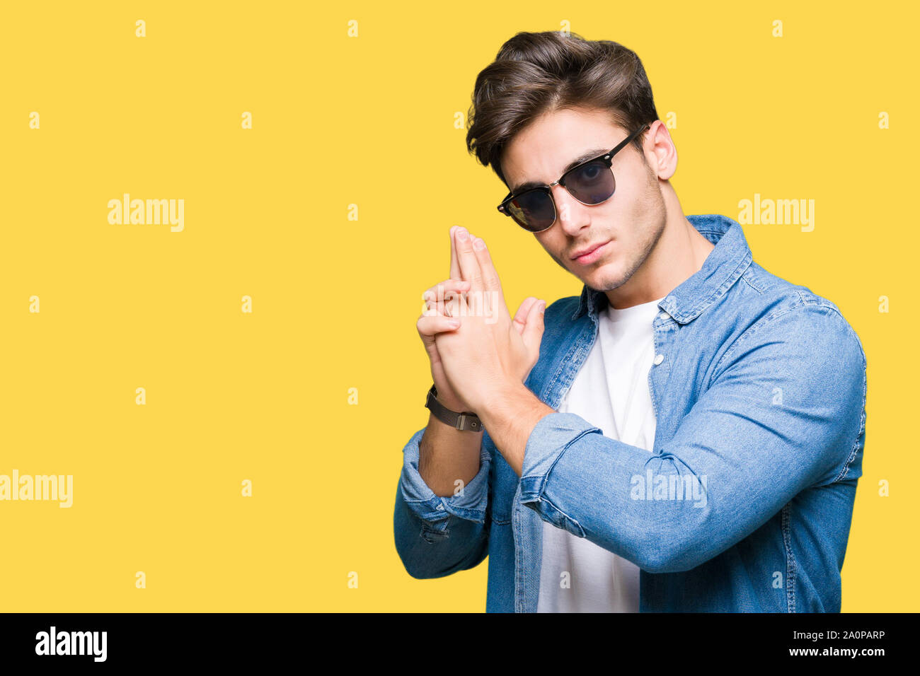 Young handsome man wearing sunglasses over isolated background Holding symbolic gun with hand