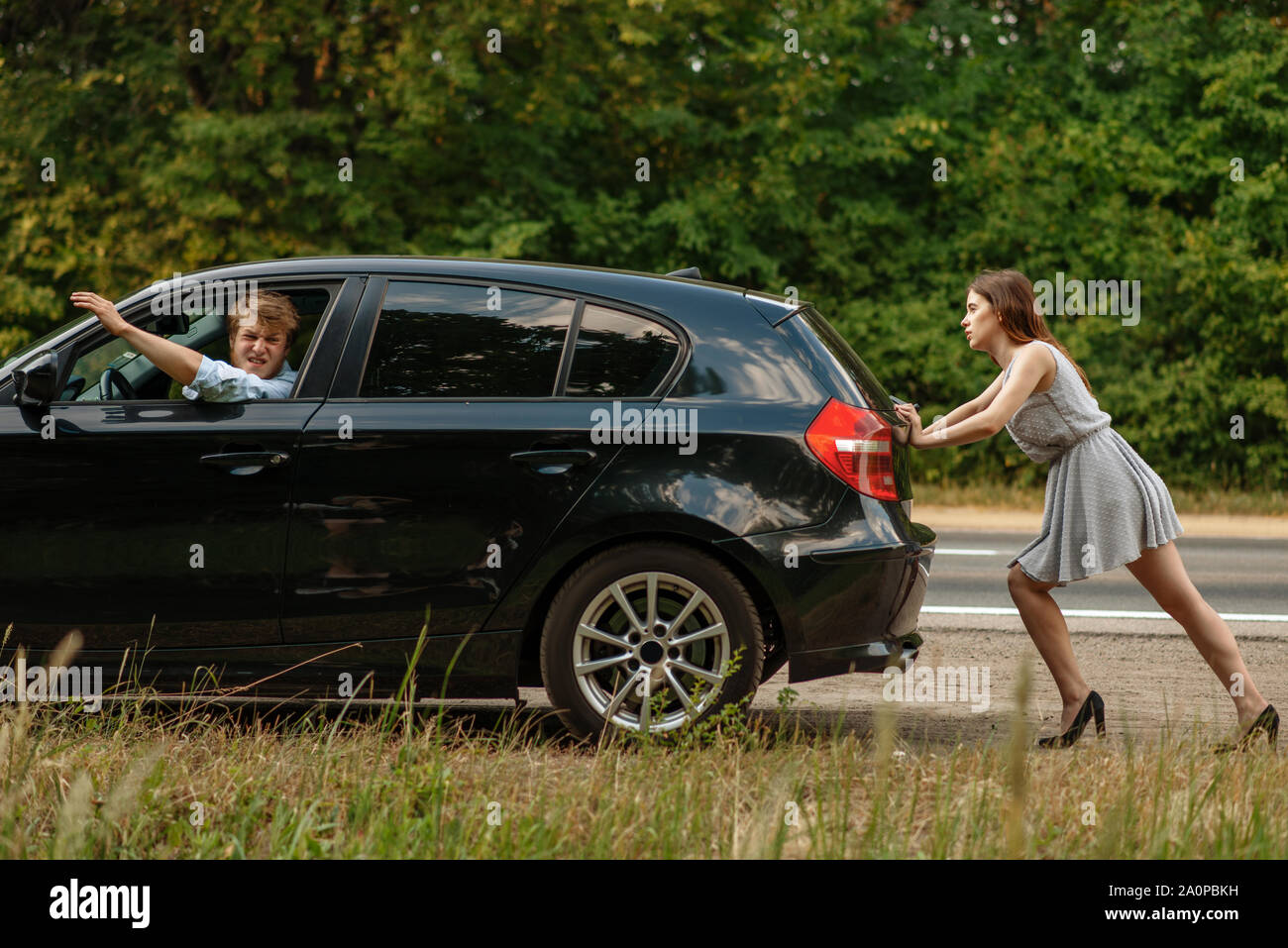 Young woman pushing broken car with man on road Stock Photo