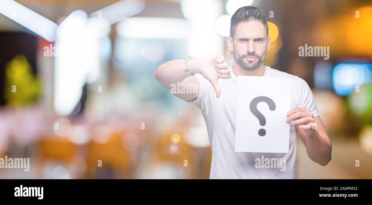 Handsome young man holding paper with question mark over isolated ...