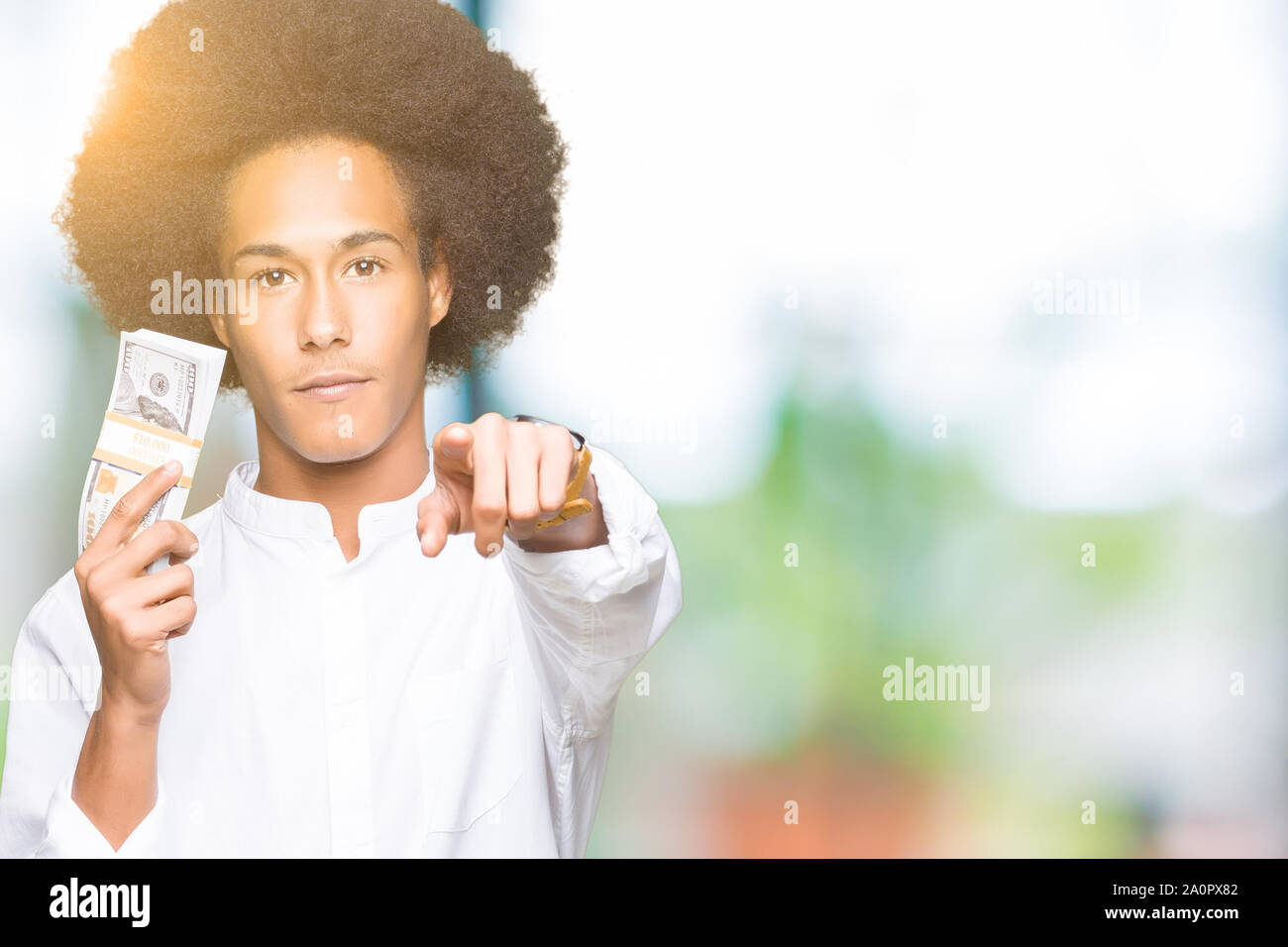 Young african american man with afro hair holding bunch of dollars pointing with finger to the camera and to you, hand sign, positive and confident ge Stock Photo