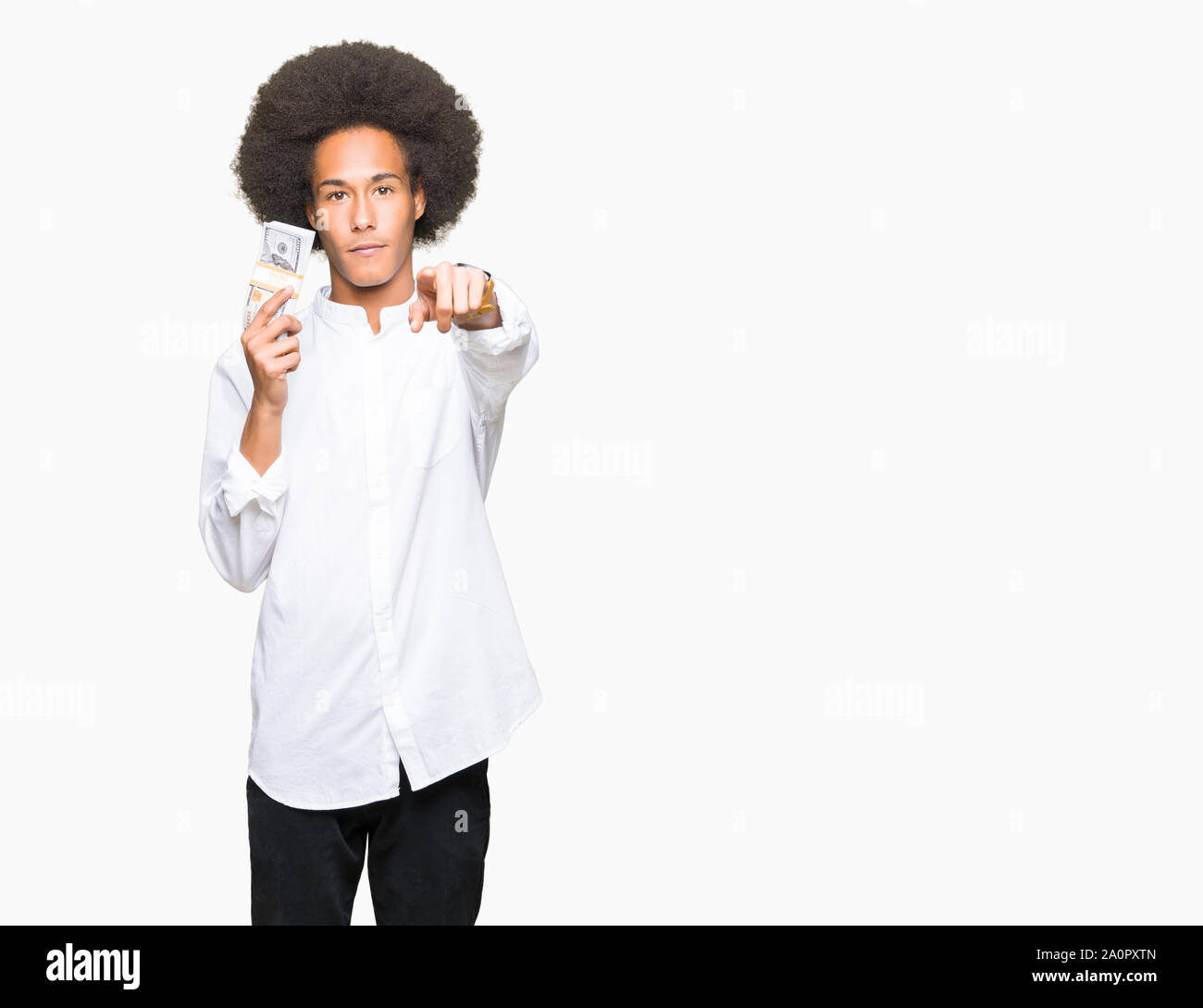 Young african american man with afro hair holding bunch of dollars pointing with finger to the camera and to you, hand sign, positive and confident ge Stock Photo