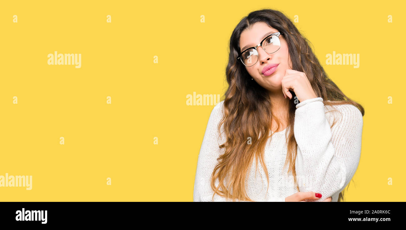 Young beautiful woman wearing glasses with hand on chin thinking about question, pensive expression. Smiling with thoughtful face. Doubt concept. Stock Photo