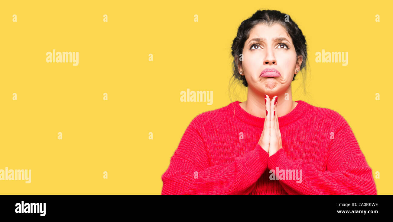 Young beautiful woman wearing red sweater and bun begging and praying ...
