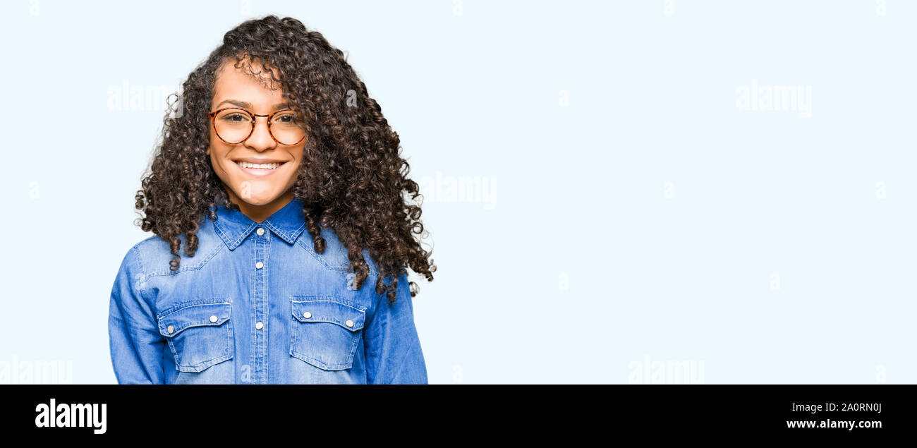 Young beautiful woman with curly hair wearing glasses with a happy and ...