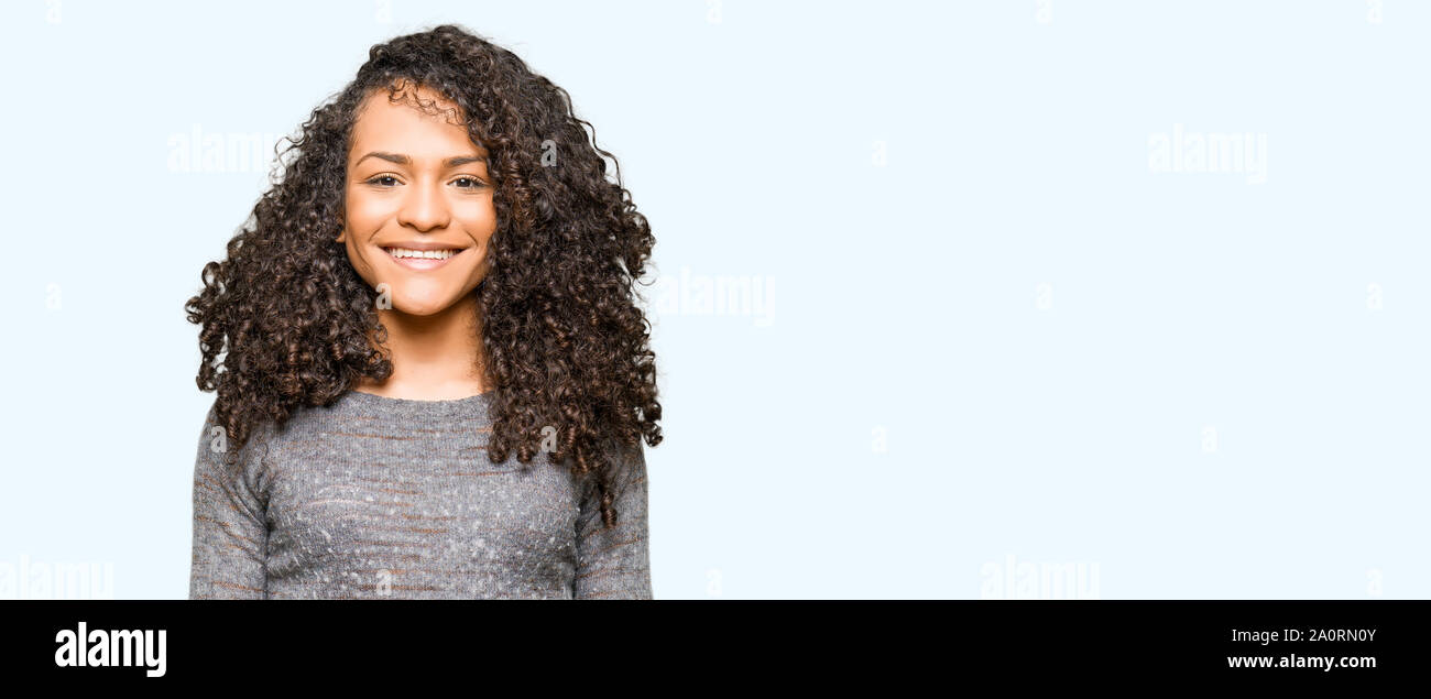 Young beautiful woman with curly hair wearing grey sweater with a happy ...