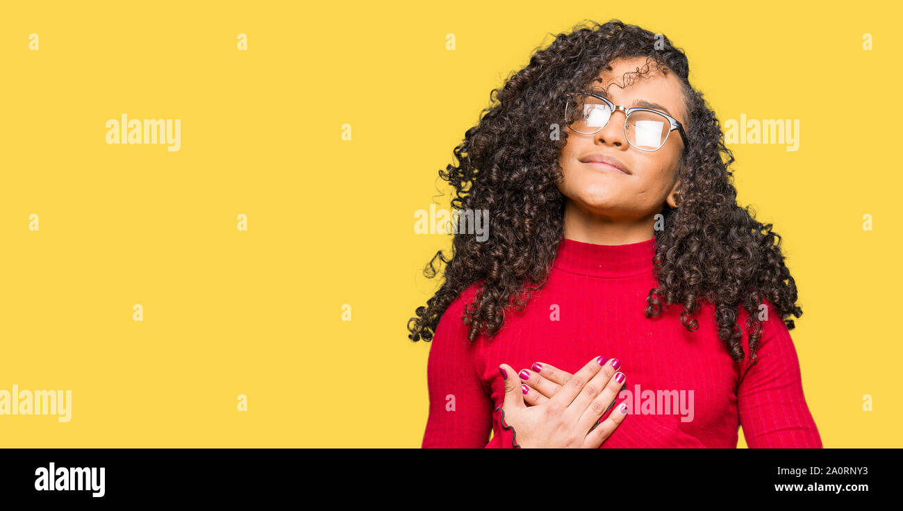 Young beautiful woman with curly hair wearing glasses smiling with ...