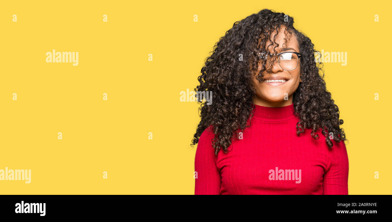 Young beautiful woman with curly hair wearing glasses with a happy and ...