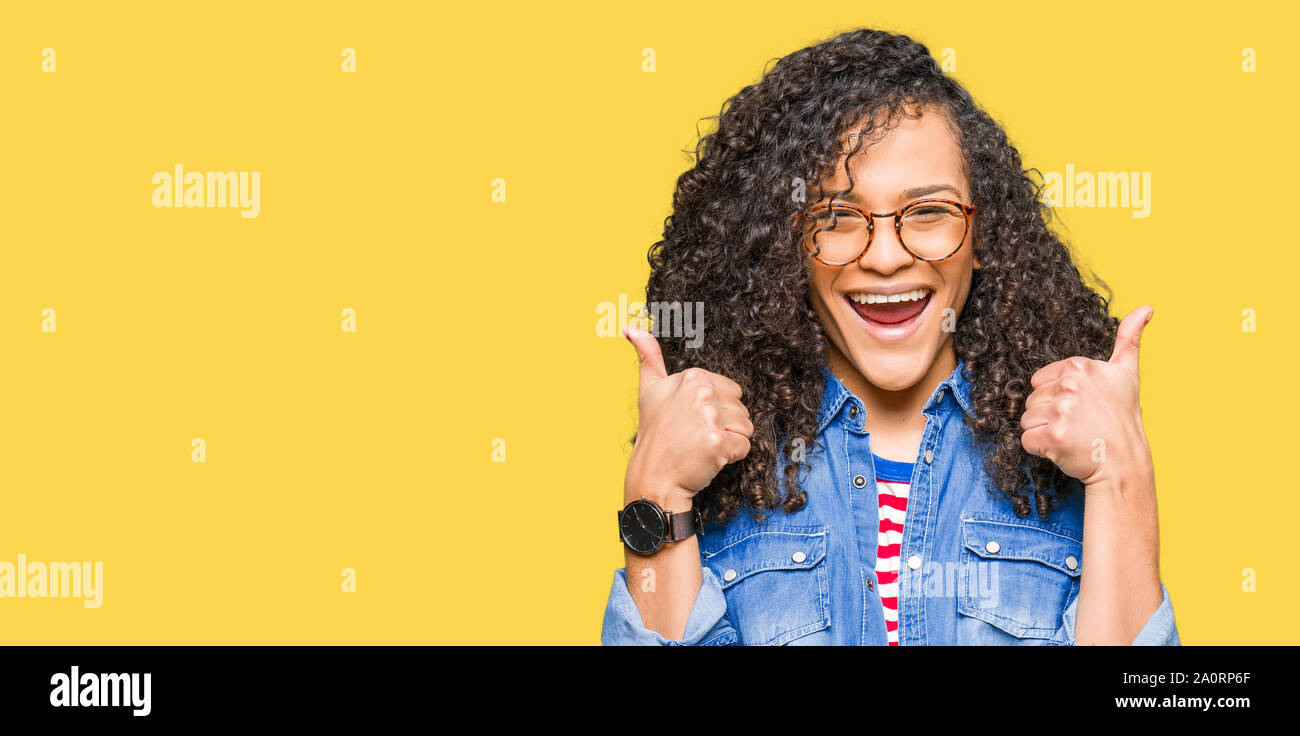 Young beautiful woman with curly hair wearing glasses success sign ...