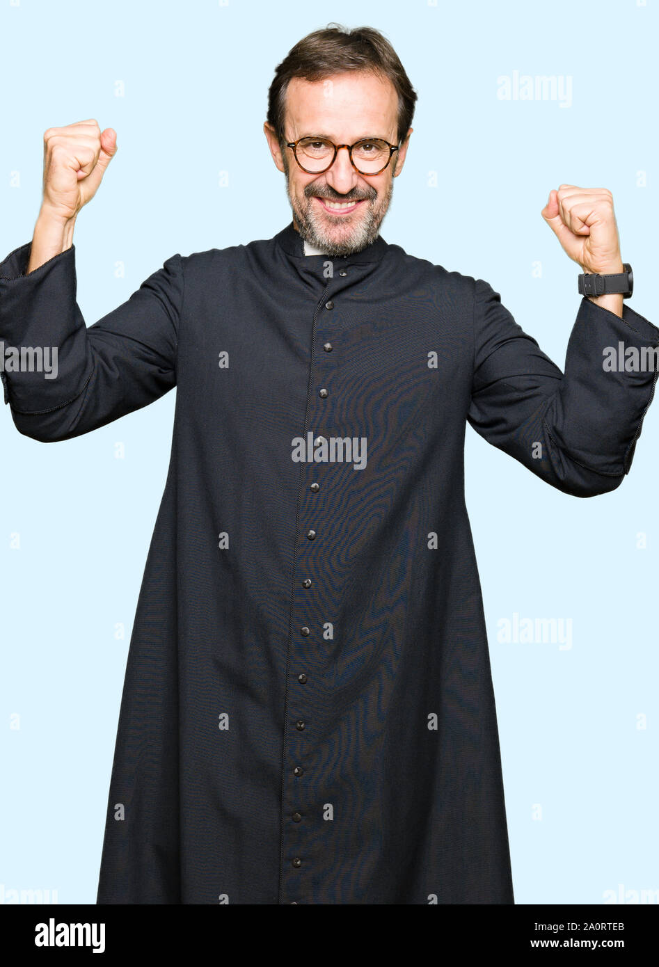 Middle age priest man wearing catholic robe showing arms muscles smiling proud. Fitness concept. Stock Photo