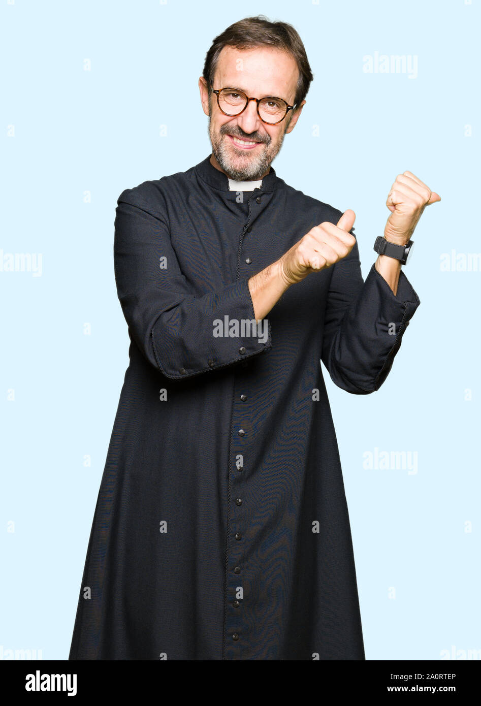 Middle age priest man wearing catholic robe Pointing to the back behind with hand and thumbs up, smiling confident Stock Photo