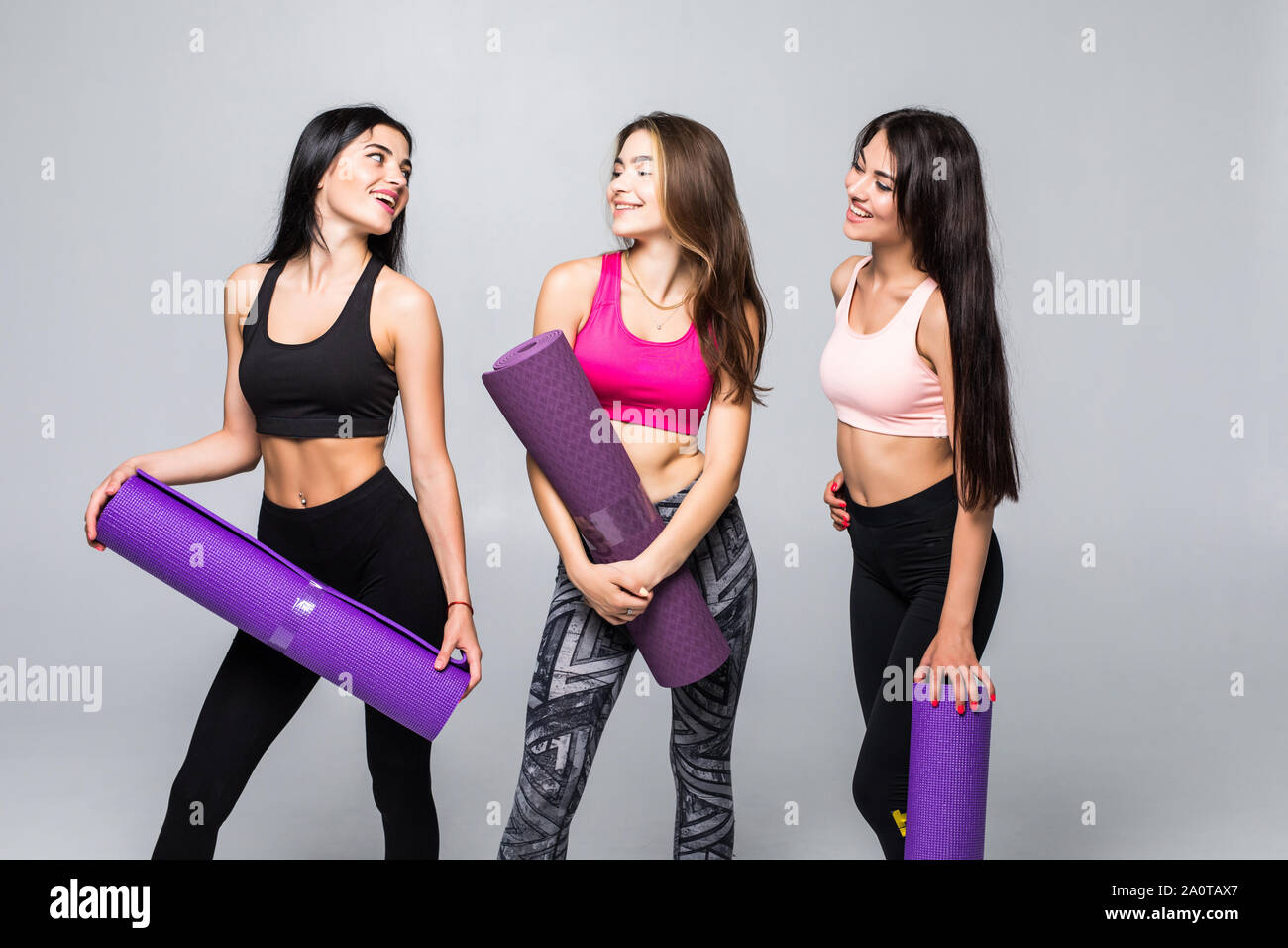 Three fitness young girls in sportswear standing against wall in