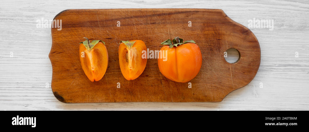 Fresh persimmon on a chopping board on white wooden background, top view. Flat lay, overhead, from above. Close-up. Stock Photo