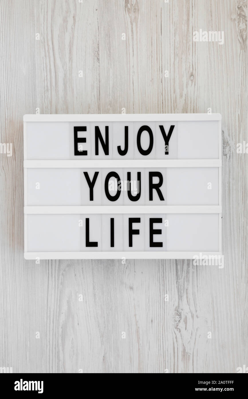 'Enjoy your life' words on a modern board over white wooden background