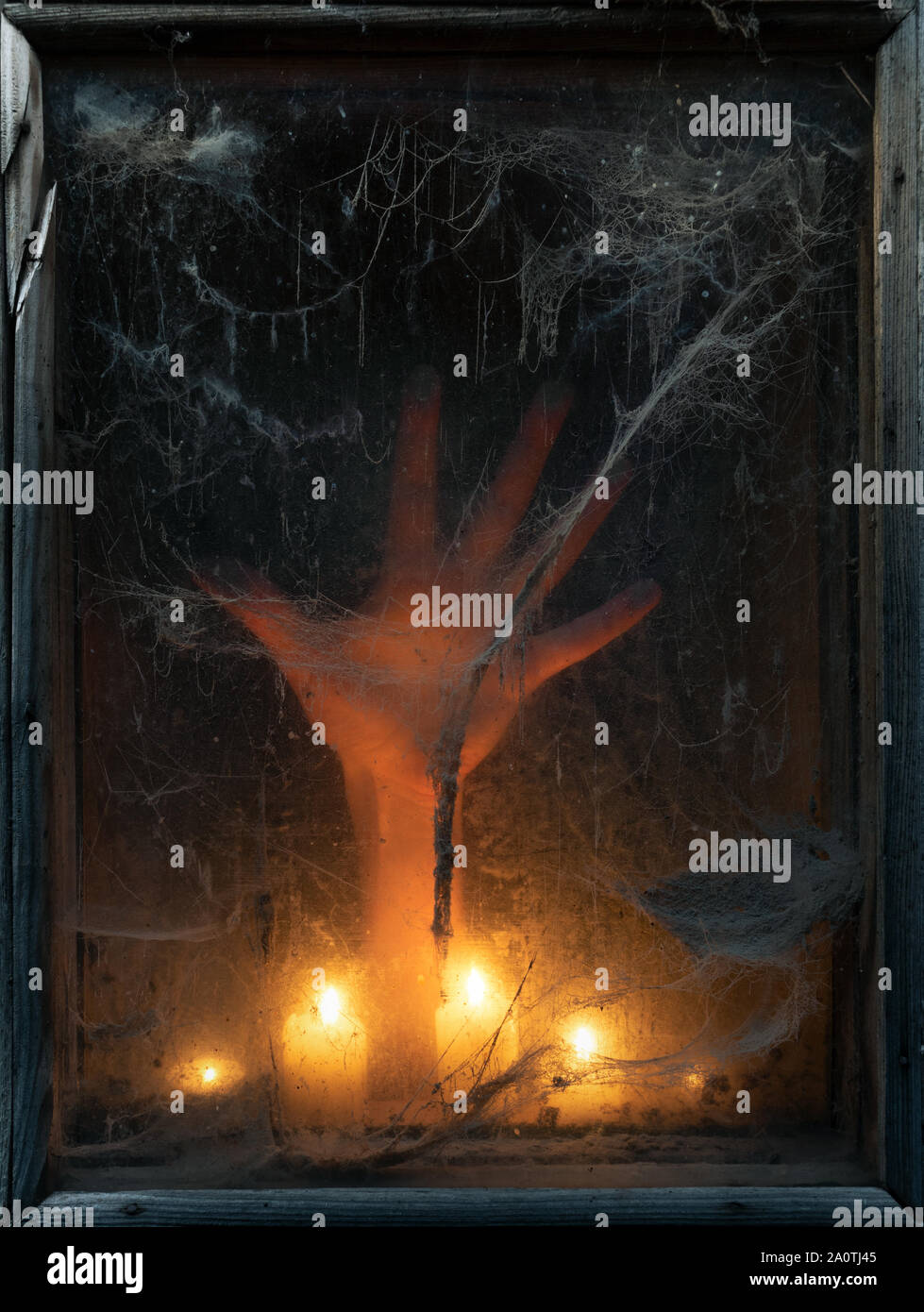 Halloween background with a scary and creepy spider web in an old window. Hand in the light of candles Stock Photo