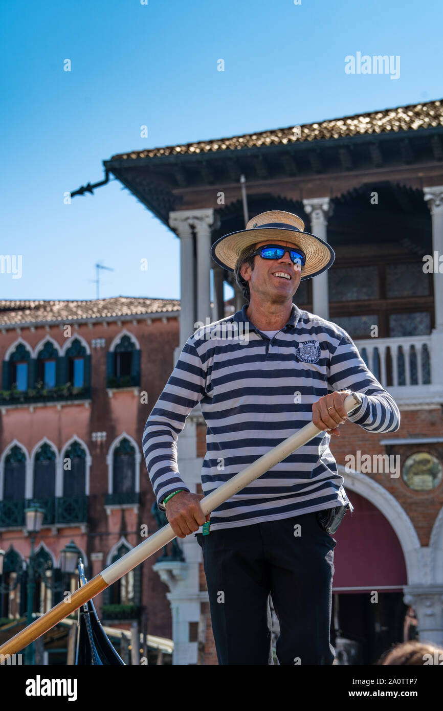 A gondolier in a traditional striped shirt and straw boater hat on a  gondola on the canals of Venice, Italy. Wearing modern mirror sunglasses  Stock Photo - Alamy