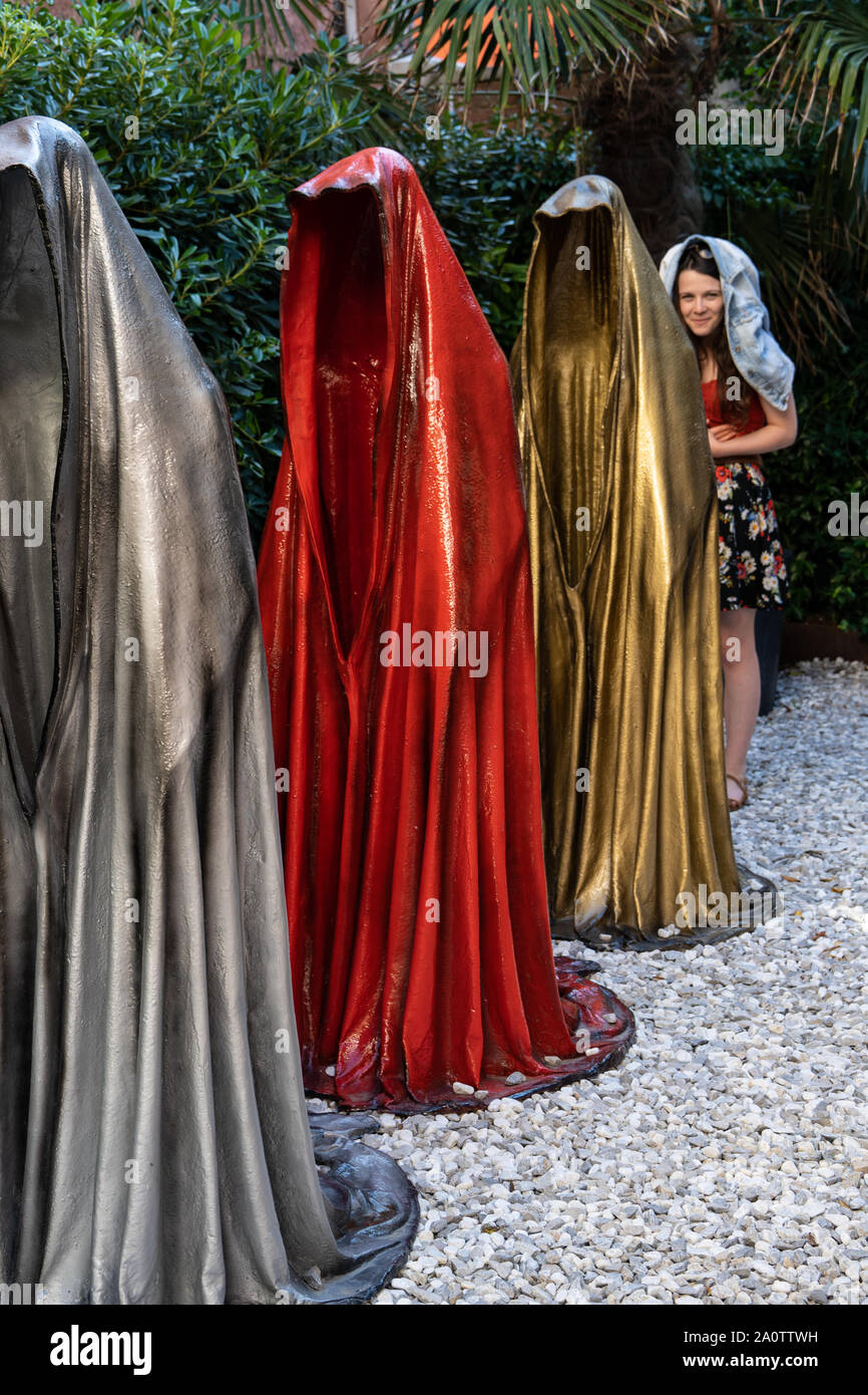 'Guardians of Time' sculpture by Manfred Kielnhofer, Venice, Italy, 2019. A girl standing in line with her coat over her head mimicking the statues Stock Photo