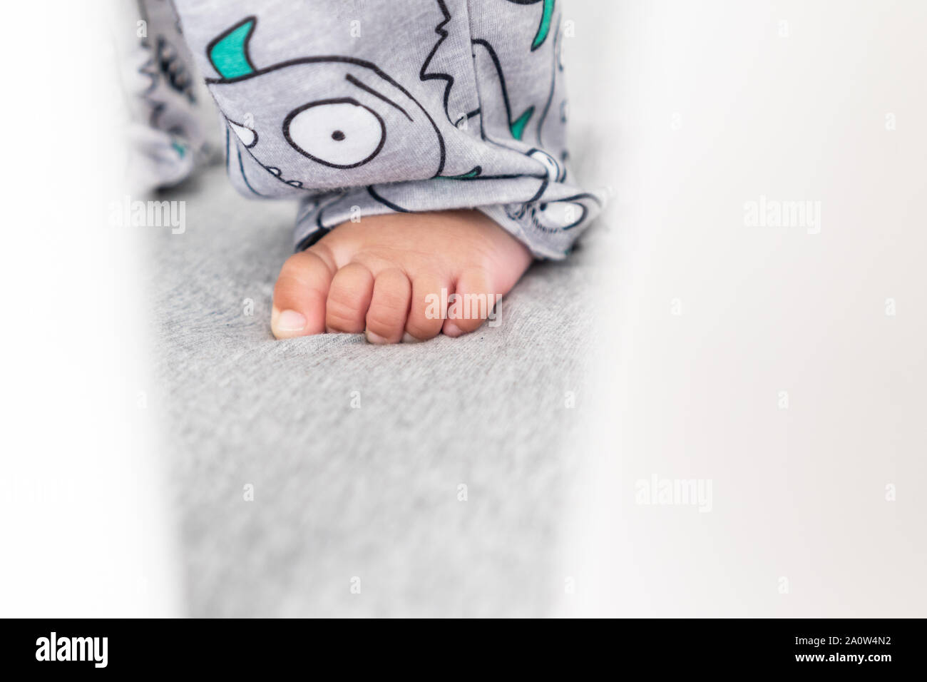 Close up of baby's feet while standing up in the crib. Wearing a cute pair of pants in a bright minimalistic modern nursery bedroom. Stock Photo
