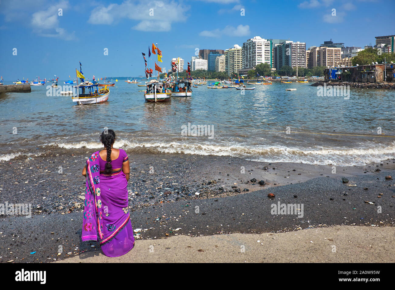 An Indian woman clad in a sari looking out over fishing boats anchored