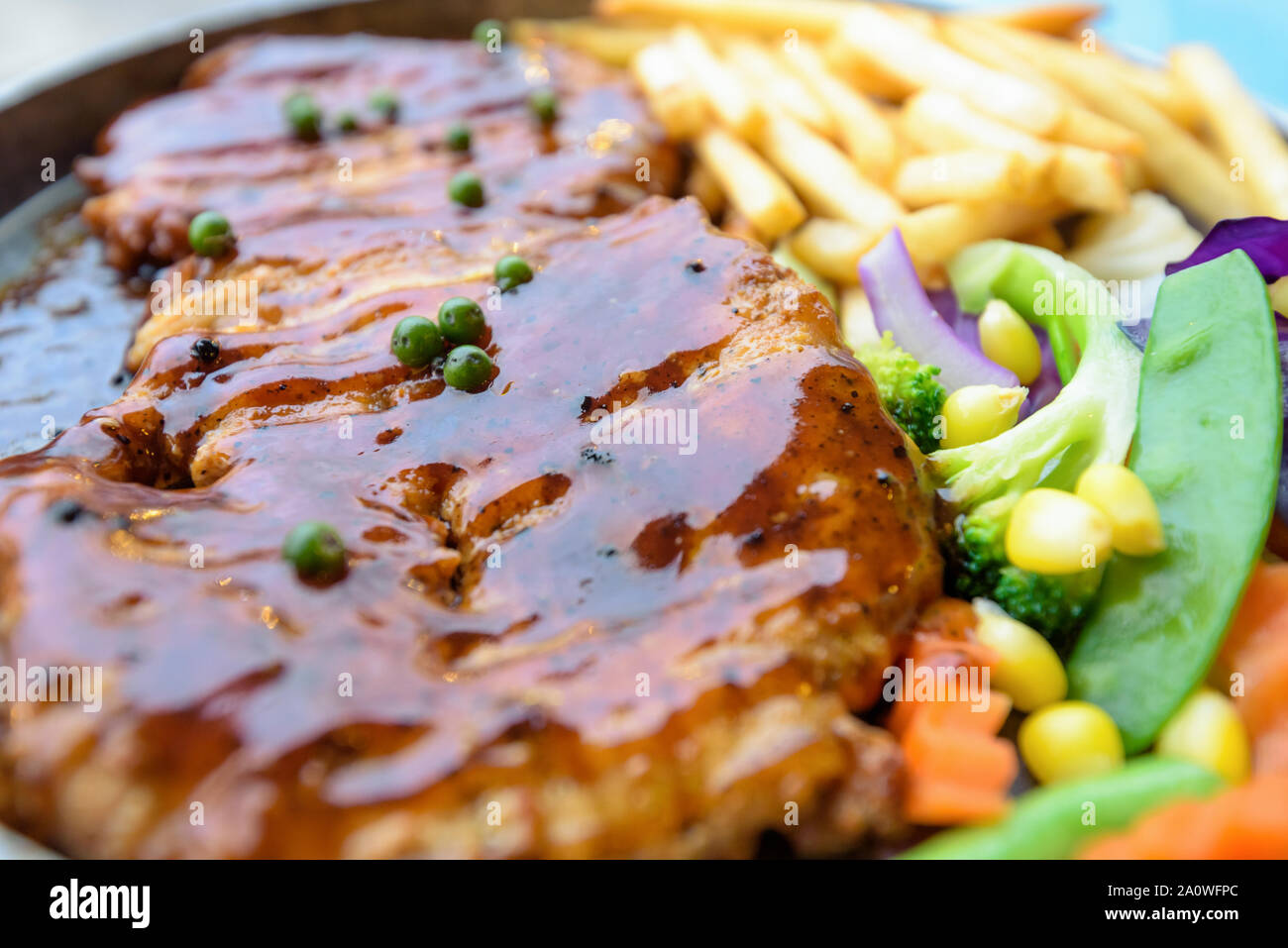 Close up of food made from grill meat, Beef steak topped with black pepper sauce on a hot plate, Dinner with vegetable salad and french fries Stock Photo