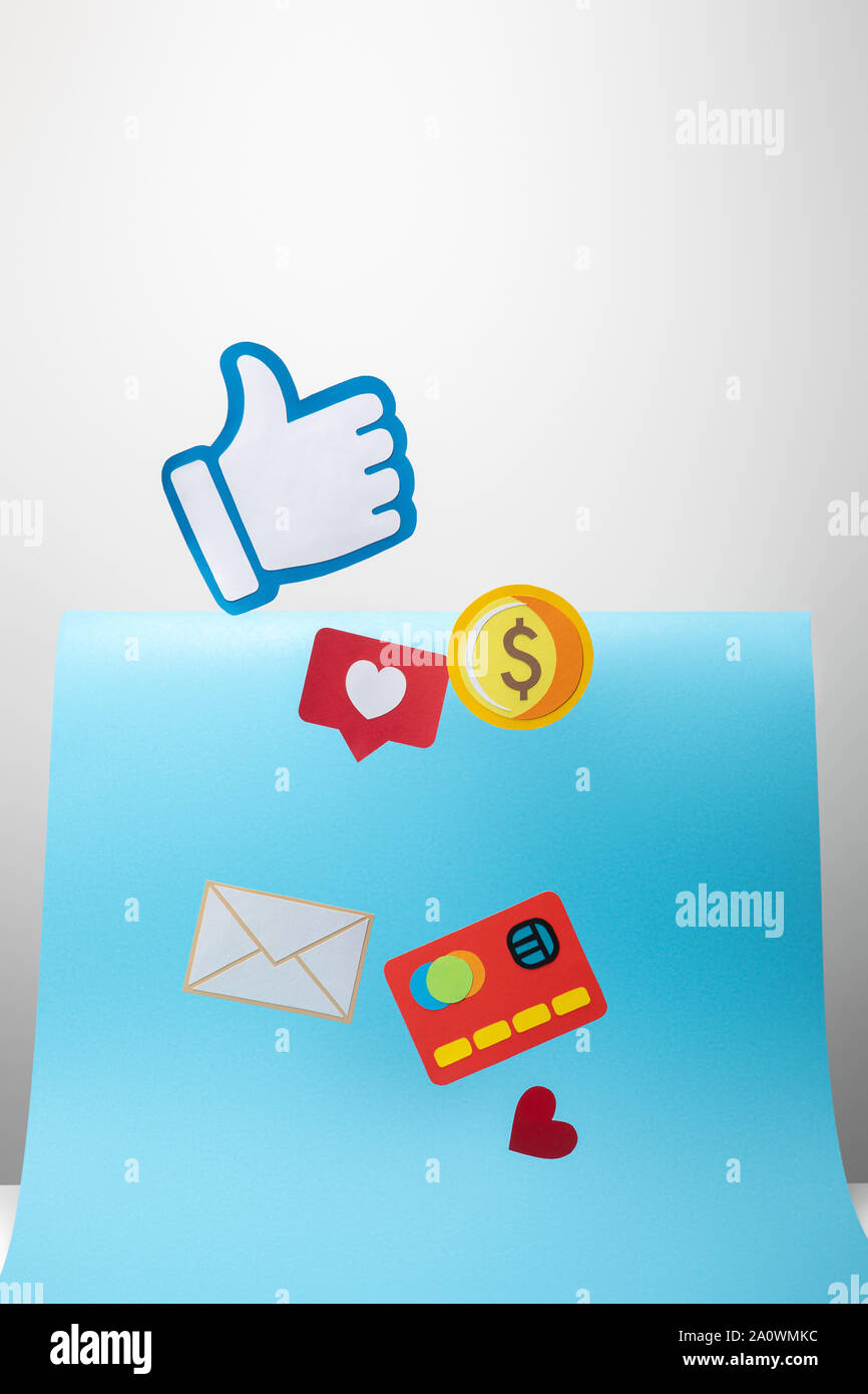 paper icons with envelope, coin, credit card, hearts and thumb up on blue and grey background Stock Photo
