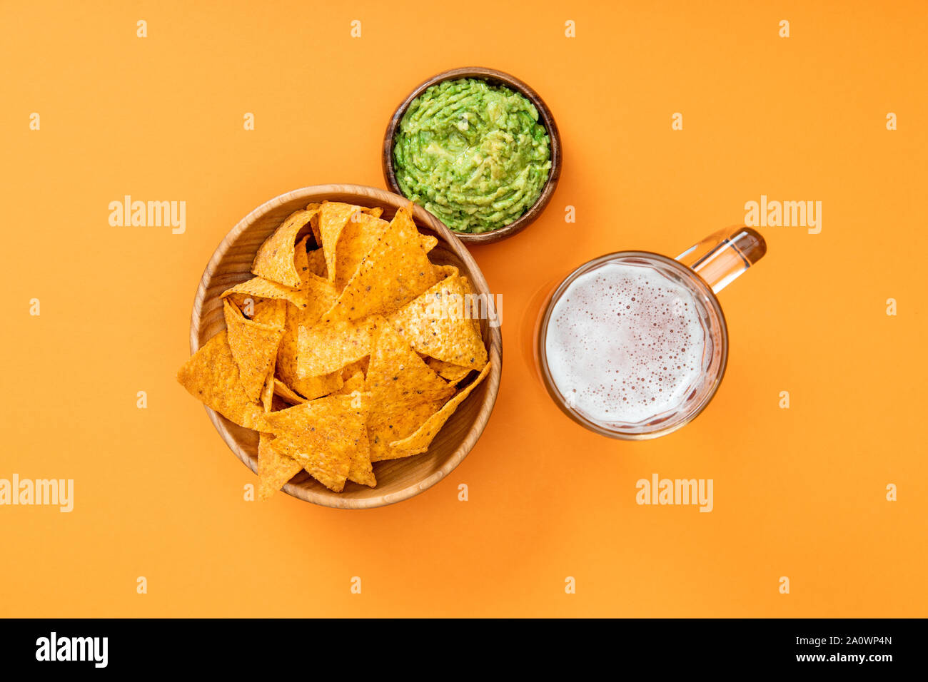 top view of crispy nachos in wooden bowl near guacamole and beer on orange background, Mexican cuisine Stock Photo