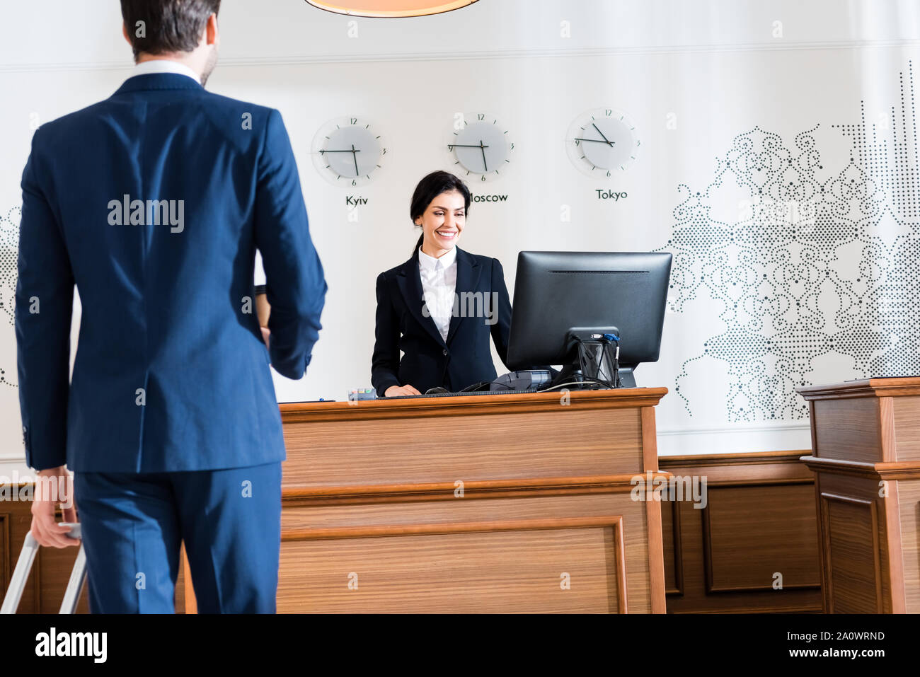 back view of businessman near cheerful receptionist looking at computer monitor Stock Photo