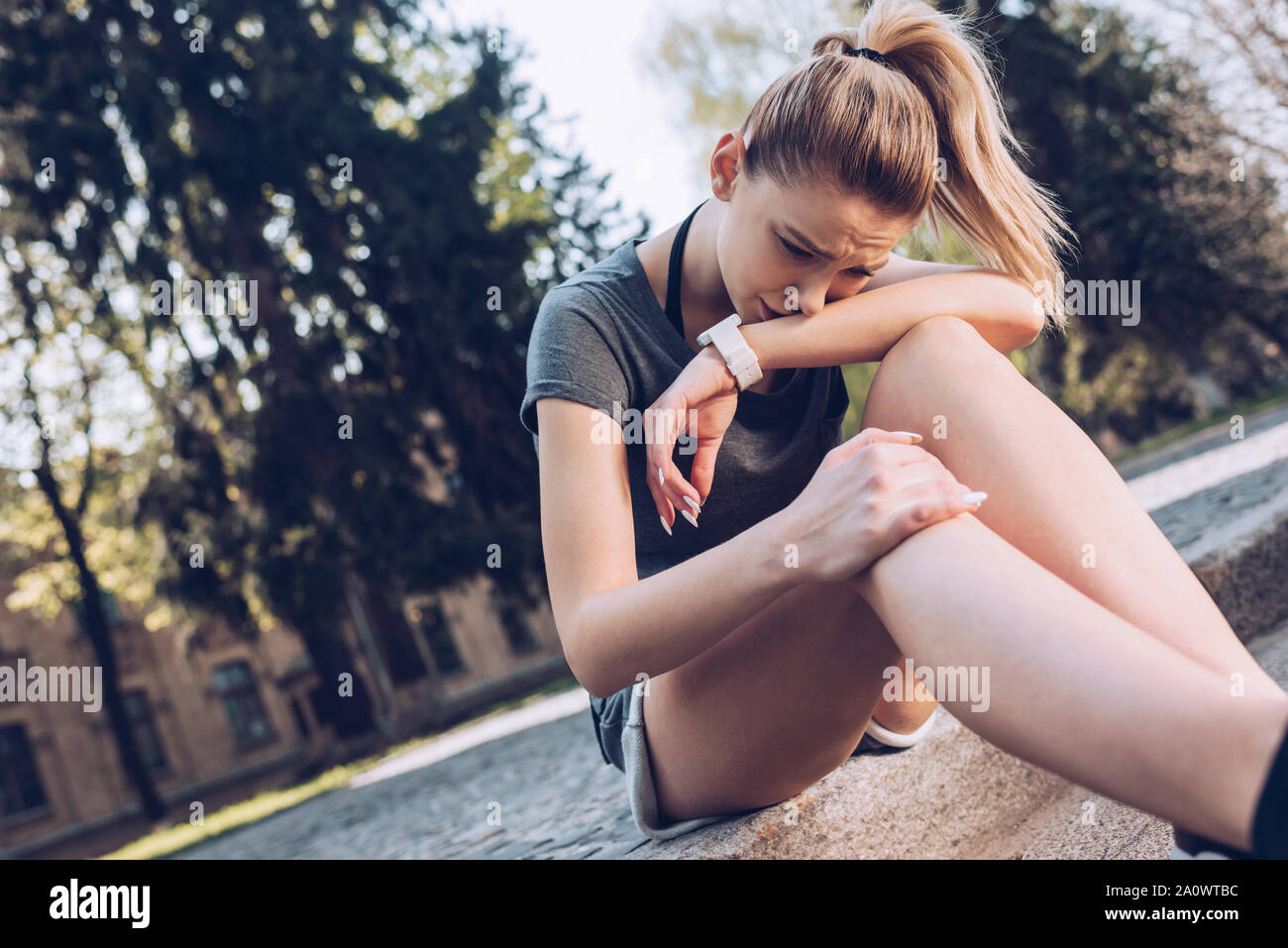 Crying Injury injured sportswoman crying while sitting on pavement and touching ...