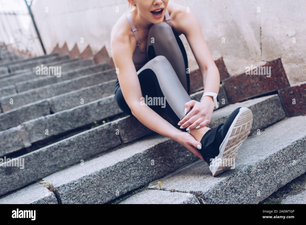 young sportswoman sitting on stairs and suffring from hurt while touching injured leg Stock