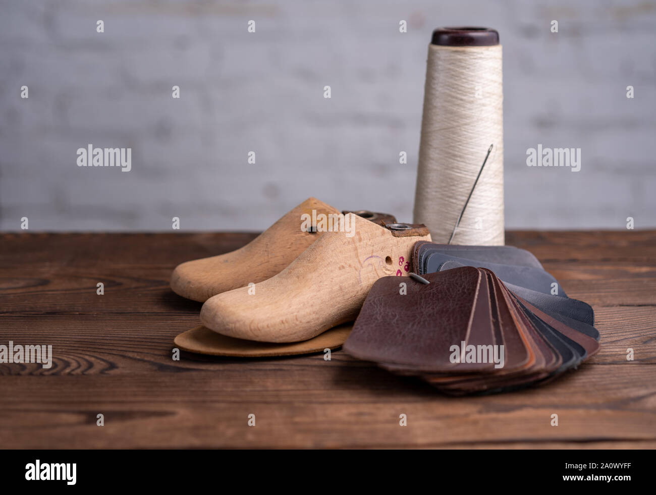 Leather samples for shoes and wooden shoe last on dark wooden table. Designer furniture clothes. Shoe maker workspace. Stock Photo