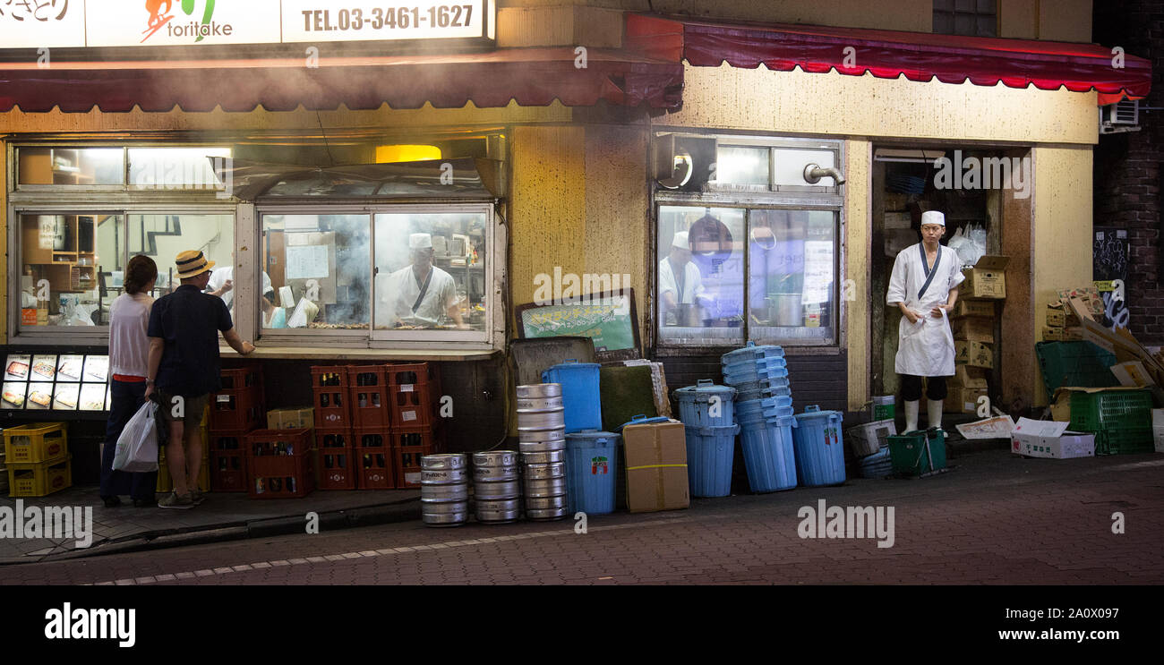 Tokyo, Japan - 21 June 2016: Back street restaurant with customers ordering at a takeaway window. Chefs in uniform are preparing food inside the kitch Stock Photo