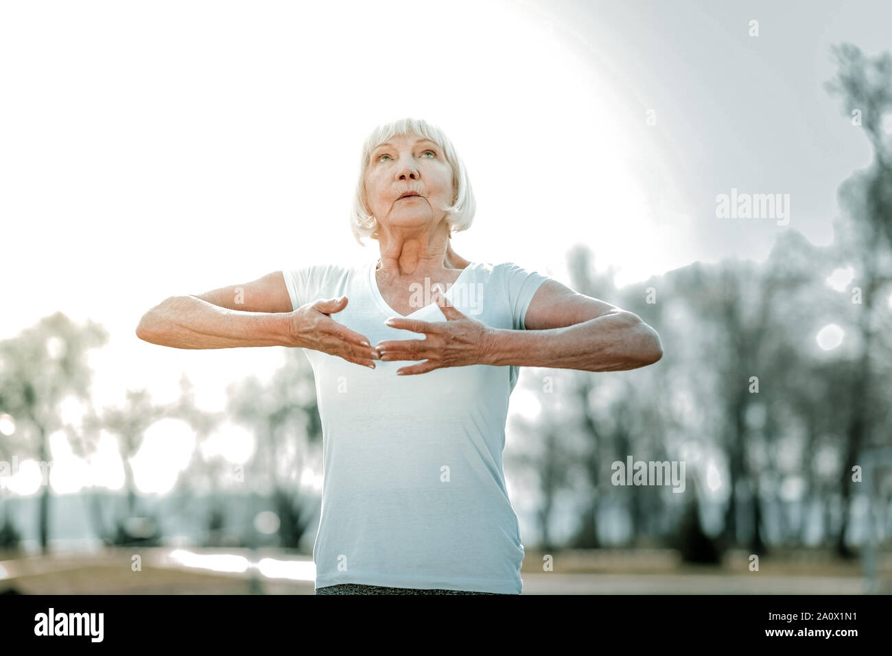 Calming elderly missis doing breathing exercises in the open air Stock Photo
