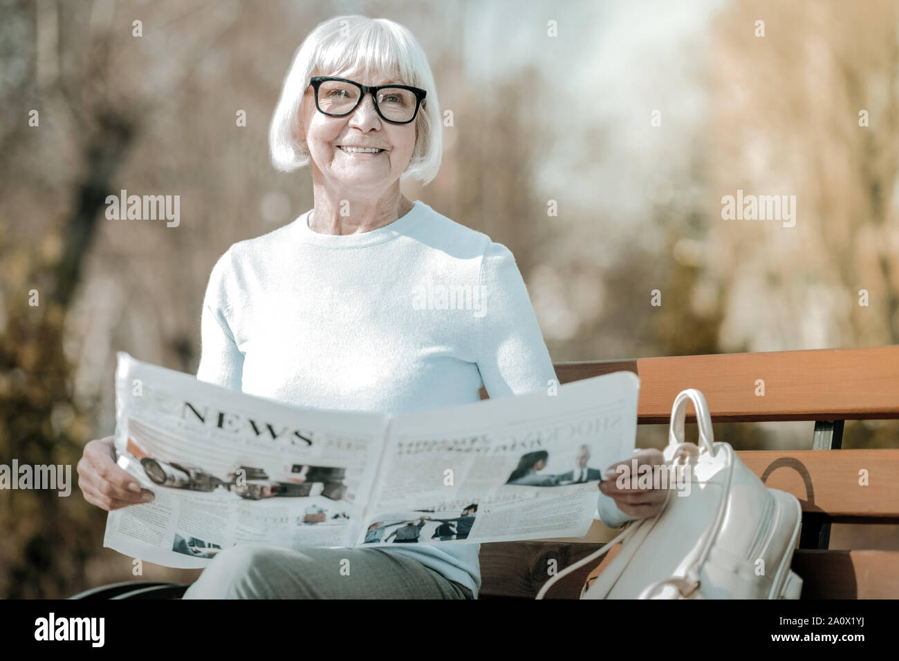 Beaming elegant elderly missis holding paper in the park Stock Photo