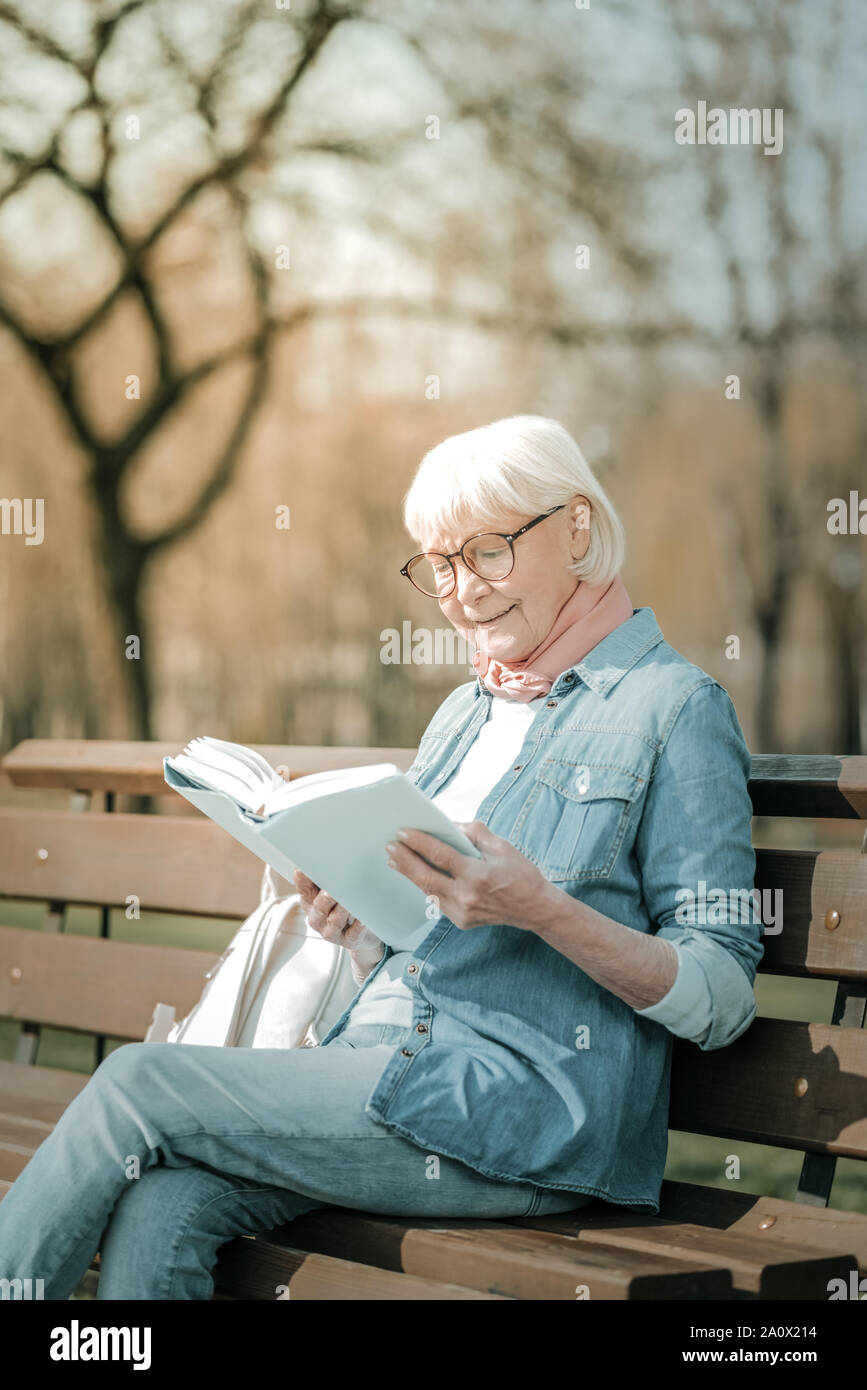 Ravishing elderly missis wearing glasses enjoying a book Stock Photo