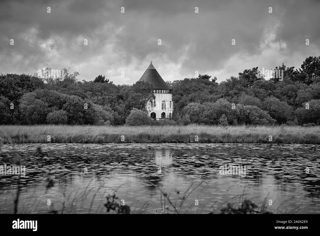 View across a lake of a round house nestled in woodland Stock Photo