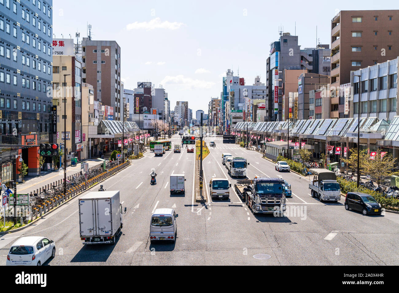 Main route, street through Sugamo town in Tokyo, Japan. View along street busy with traffic from overhead bridge. Buildings on either side. Stock Photo