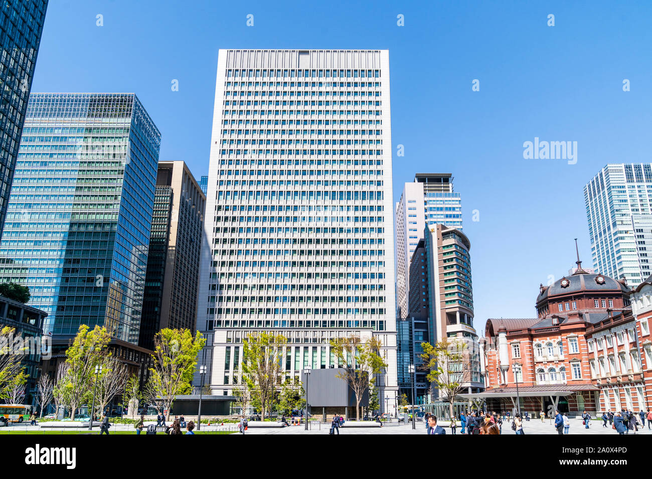 Tokyo, the 28 story skyscraper, Nihon Seimei Marunouchi Building on a springtime day. Foreground, people, trees and part of Tokyo station. Blue sky. Stock Photo